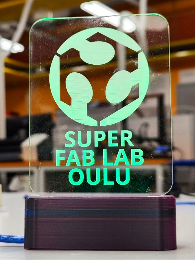 Spot Price Lamp: an acrylic panel engraved with the Super Fab Lab Oulu logo, lit green